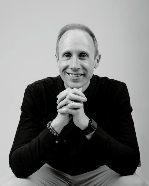 A photo of Brendon Orr sitting down smiling with his chin wresting on his hands. 